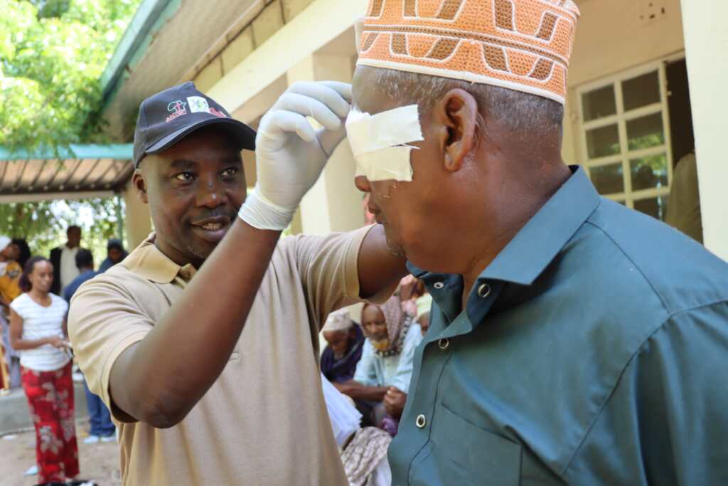 A man with gloves, removing an eye patch from a patient